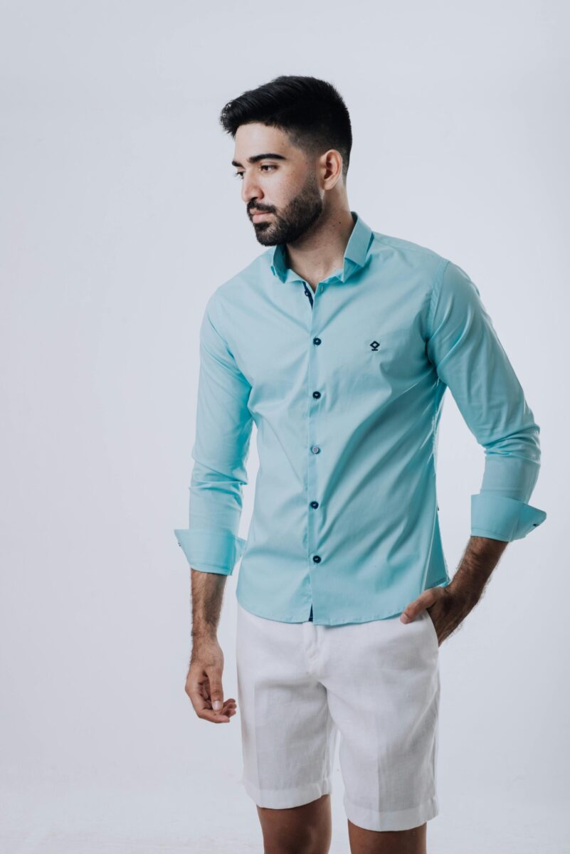 Fashionable man posing in a blue shirt and white shorts on a plain background.